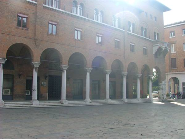 Brick loggia with arches and stone columns in the square, strong sunlight