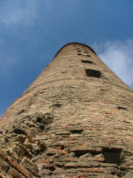Ancient brick tower with weathered walls, shot from below against blue sky
