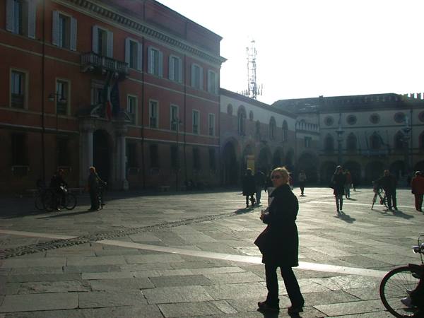 Tourist in black coat crossing the paved square among historic buildings