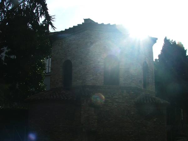 Arian Baptistery in Ravenna, ancient brick backlit by sun among trees