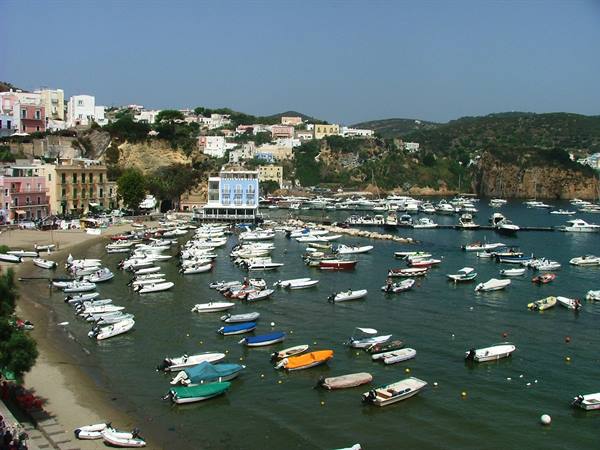 Dozens of small boats moored at Ponza harbor, colorful houses on the hillside