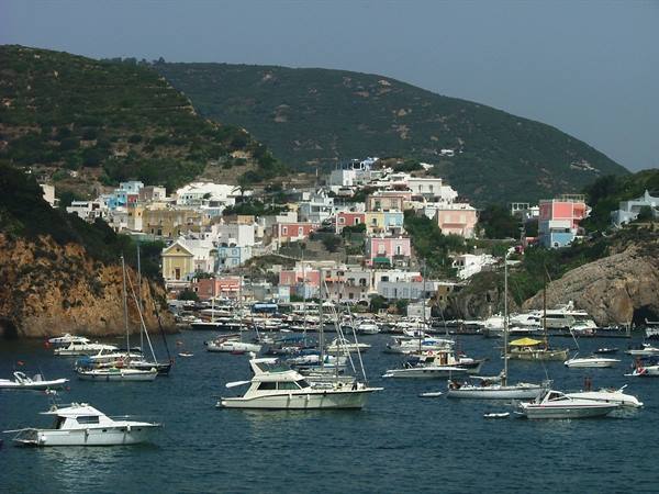 Boats moored at Ponza harbor among colorful houses and green hills