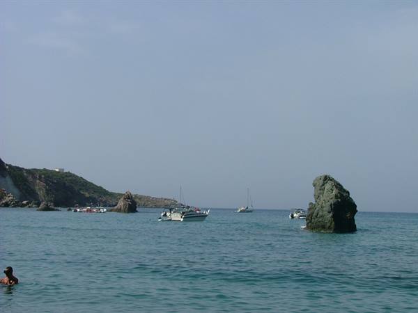Swimmers and boats in a green cove with sea stacks on turquoise water