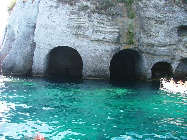 Boats in front of caves carved into limestone rock, turquoise sea