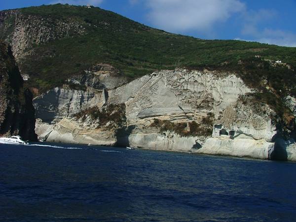 white tuff cliffs above blue sea, a motorboat speeds past