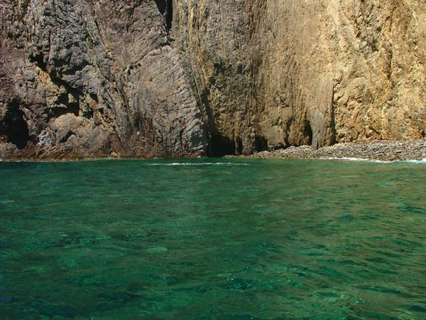 Emerald green water at the base of tall yellowish rock cliffs
