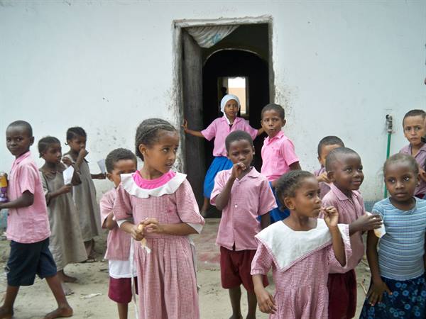 Children in pink uniforms outside a whitewashed school doorway