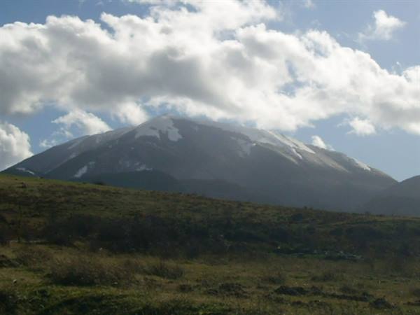 Snow-capped mountain under white clouds above grassy hills