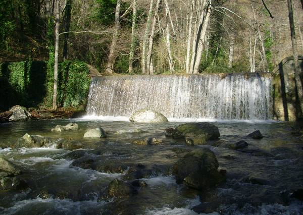 Man-made waterfall over river with boulders, bare woodland behind