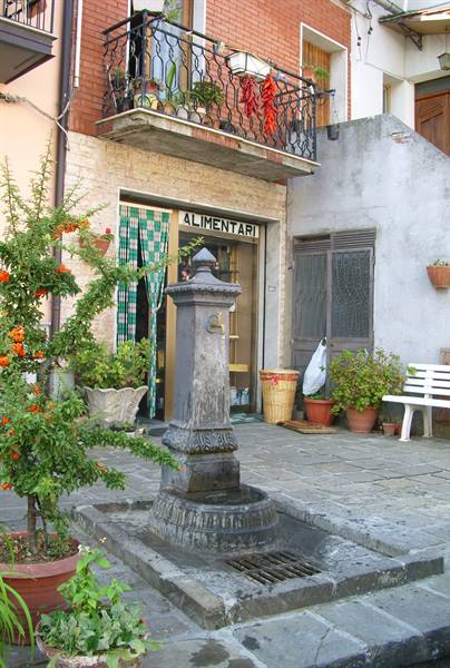 Stone fountain in front of an alimentari shop with chili peppers hanging from the balcony