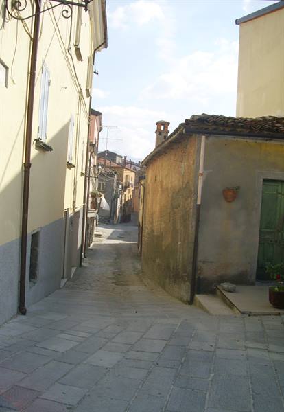Paved alley between plastered houses and a weathered stucco building, morning light
