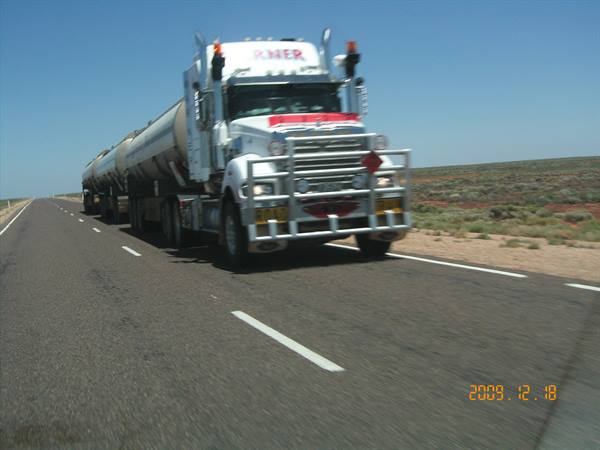 White tanker truck overtakes on highway through desert scrub, clear blue sky