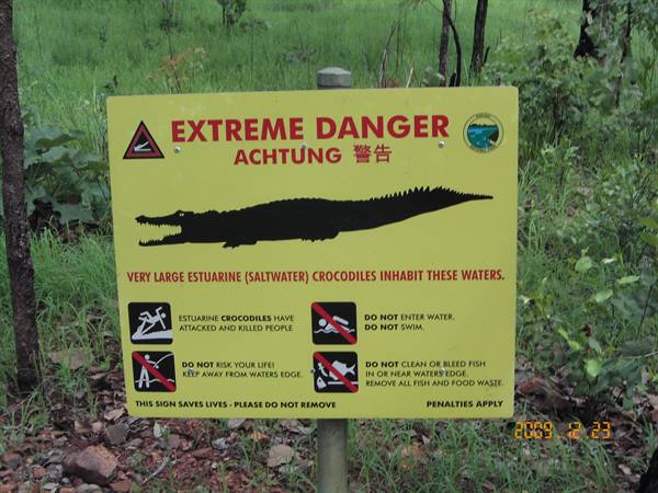 Yellow crocodile danger warning sign among green grass and trees