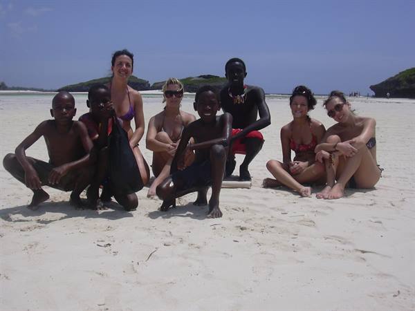 Tourists and local boys crouching on white sand, sunny tropical beach