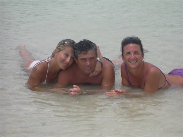 Three friends in swimsuits lying in shallow clear water, smiling together