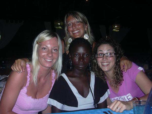 Four smiling friends hugging at a table at night, flash lighting