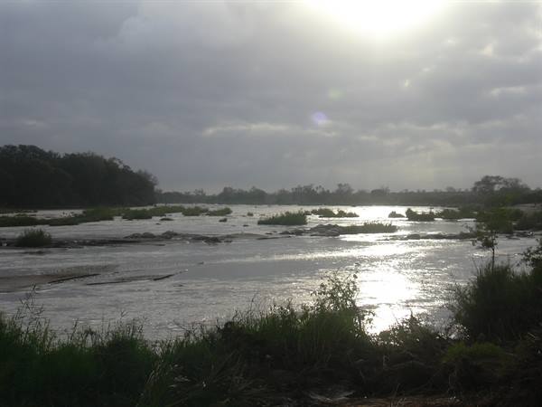Wide river with rocks and vegetation, sunlight breaking through clouds