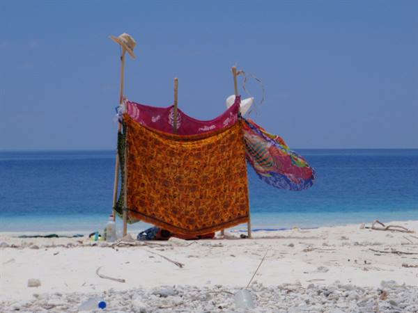 Colorful cloths on wooden poles shelter from the sun on white sand