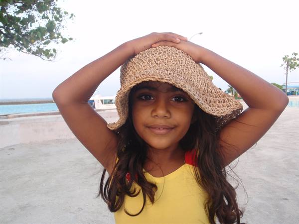 Girl in yellow top holds a straw hat on the sandy beach
