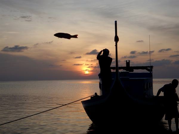 Fisherman silhouetted on a wooden boat at sunrise over calm sea