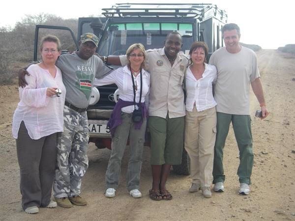 Smiling tourists and guide posing in front of safari jeep on dirt road