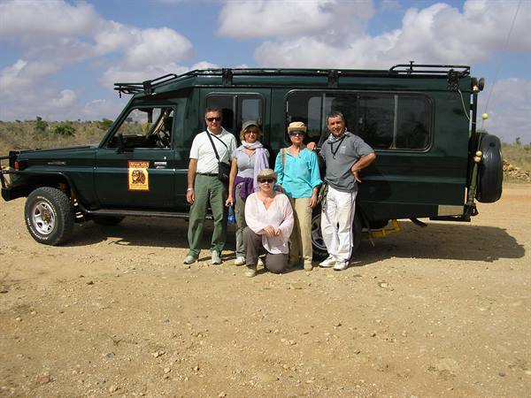 Five tourists beside a green safari Land Cruiser on sandy track