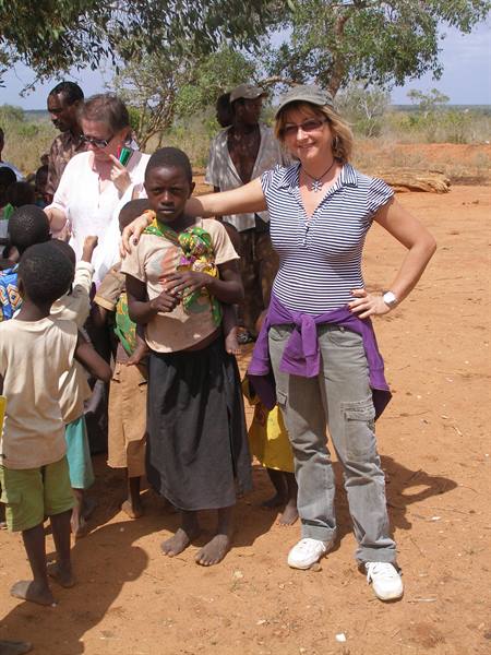 Tourist with arm around local girl among groups of children on red dirt