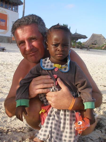 Shirtless tourist hugs a little girl in a checkered dress on the beach
