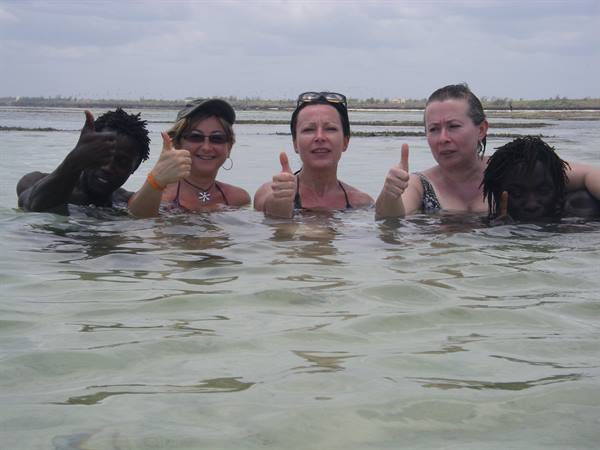 Four people in the sea, three giving thumbs up, cloudy sky