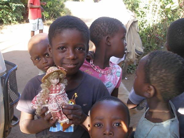 Children on a dirt road, one smiling while holding a doll
