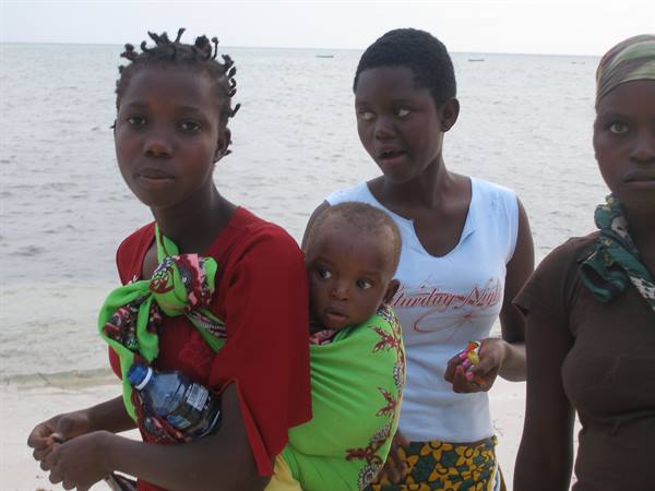 Women and a child on the beach, one carrying a baby on her back