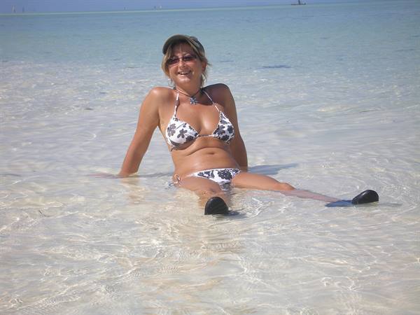 Woman in a bikini sitting in clear turquoise water on a tropical beach