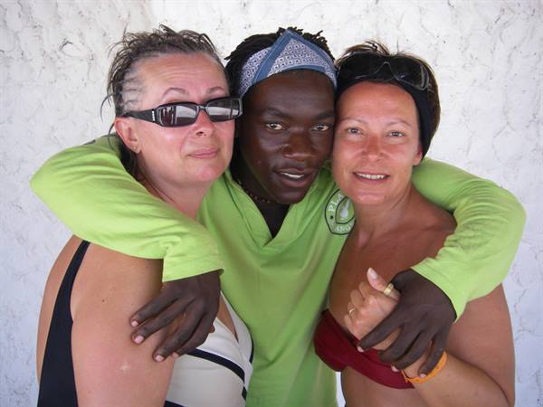 Three friends hugging and smiling in front of a white sunlit wall