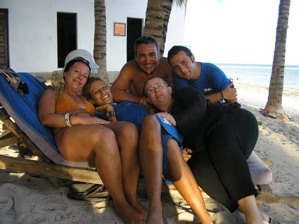 Five friends hugging on a wooden lounge chair under palm trees