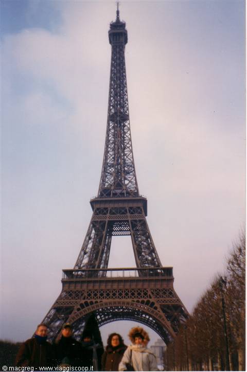 Tourists walk past the iron Eiffel Tower under a cloudy Paris sky