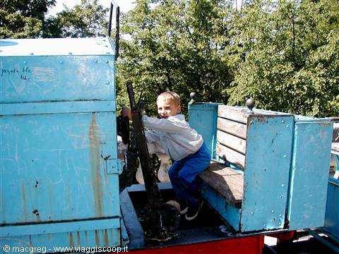 Child climbing on a small blue steam locomotive in a leafy park