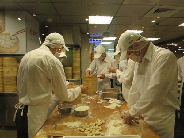 Chefs in white hats making steamed dumplings, bamboo steamers on counter
