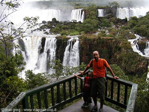 Man and child on wooden balcony in front of Iguazú Falls