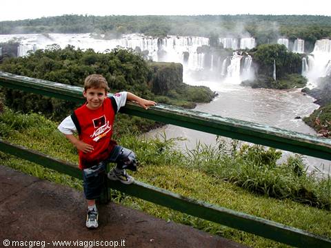 Boy leaning on green railing in front of Iguazu Falls