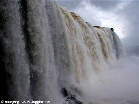 Massive falls of brown water and white foam, gray sky, mist
