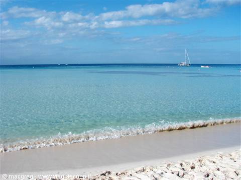 Foamy wave on white sand, turquoise sea, sailboats in the distance