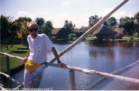 Tourist with yellow fanny pack on wooden bridge, thatched huts over tropical lagoon