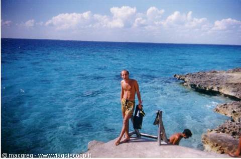 Man in yellow trunks holding snorkel gear on limestone rocks, turquoise sea