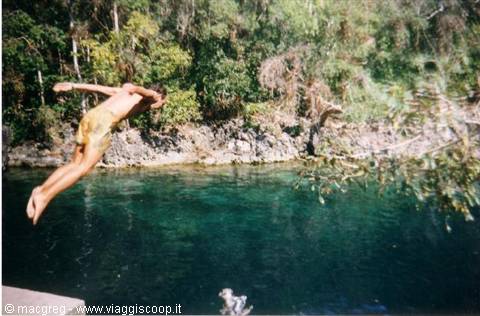 Boy diving headfirst into emerald water surrounded by rocks and trees
