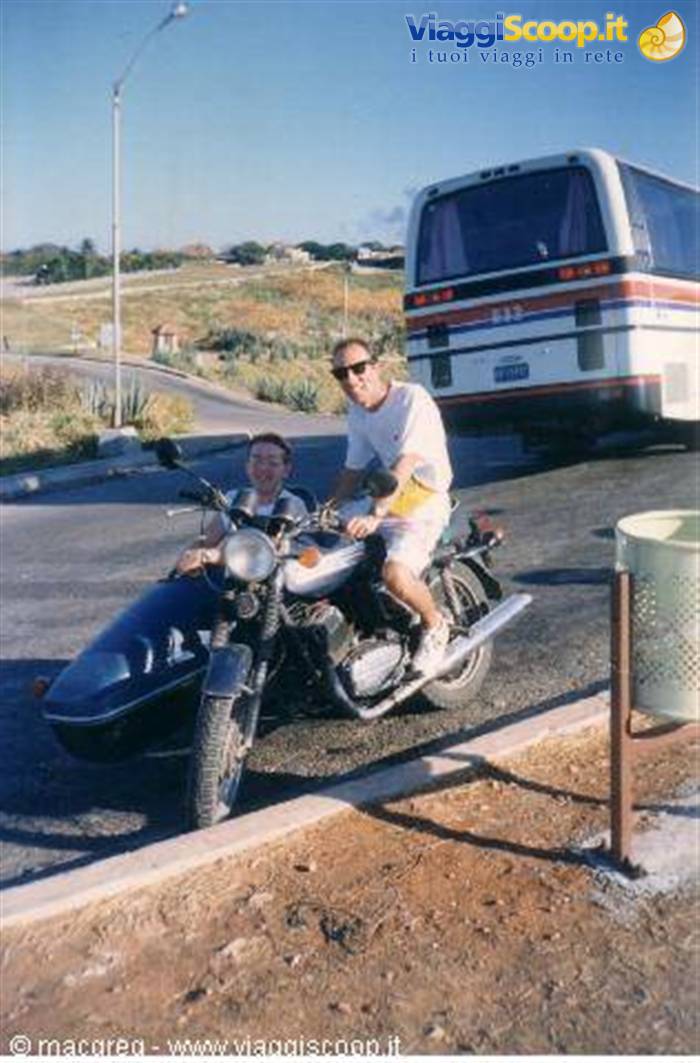 Two men on a motorcycle with blue sidecar beside a bus