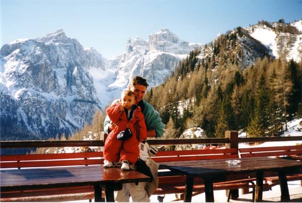 Man holding child in red snowsuit before snowy Dolomites peaks