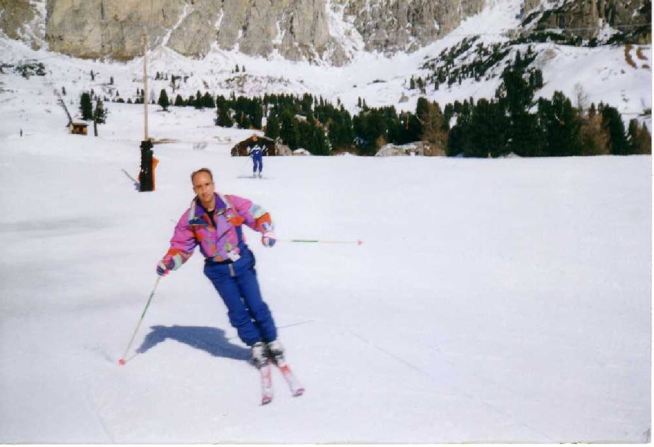 Man in colorful suit skiing on snow, rocky mountains behind