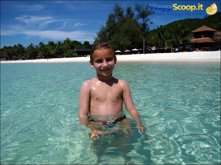 Smiling boy in turquoise water in front of white beach and palms