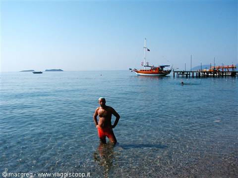 Man in red swimsuit standing in clear water, boats and pier behind