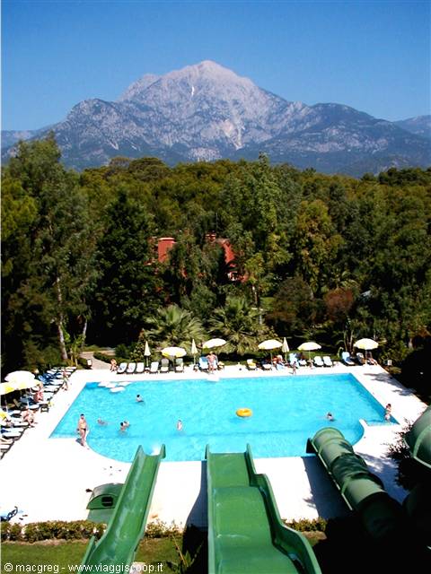 Pool with green slides, umbrellas and swimmers, Tahtalı mountain rising behind